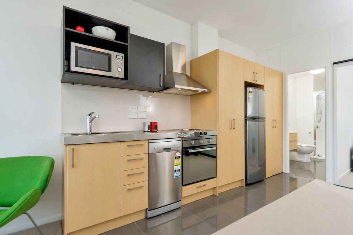 A modern kitchen with stainless steel appliances, wooden cabinets, and a green chair.
