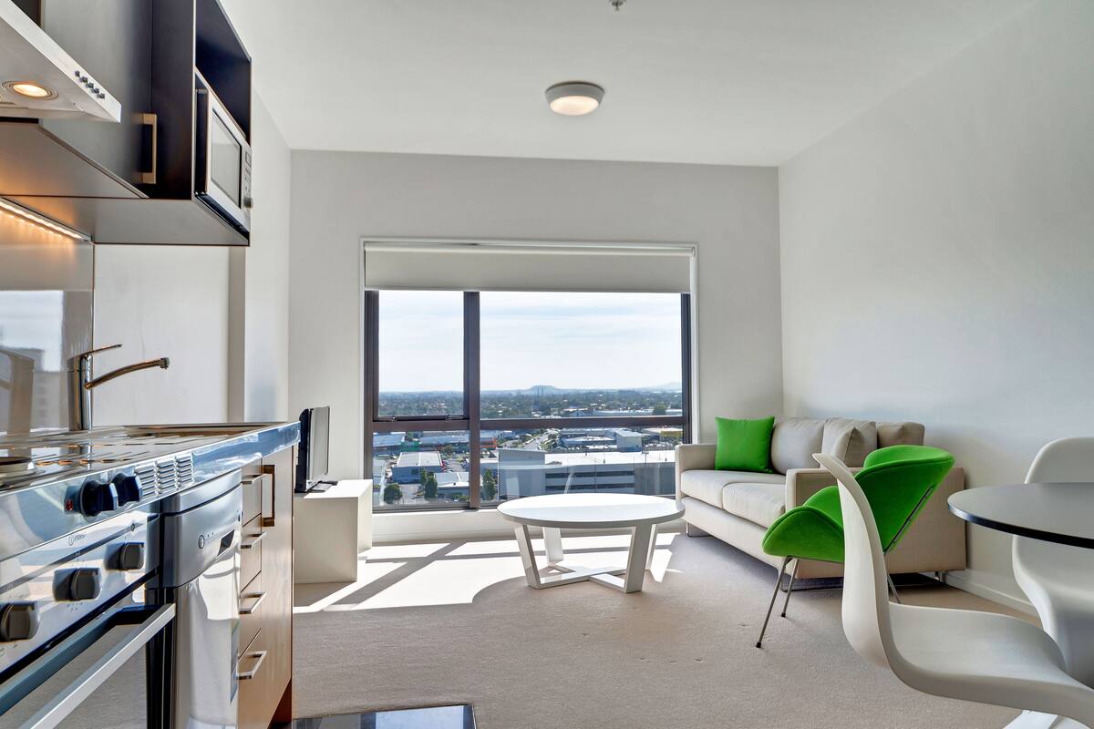 A modern apartment with a kitchen, a balcony with a city view, and a living area with a sofa and chairs.
