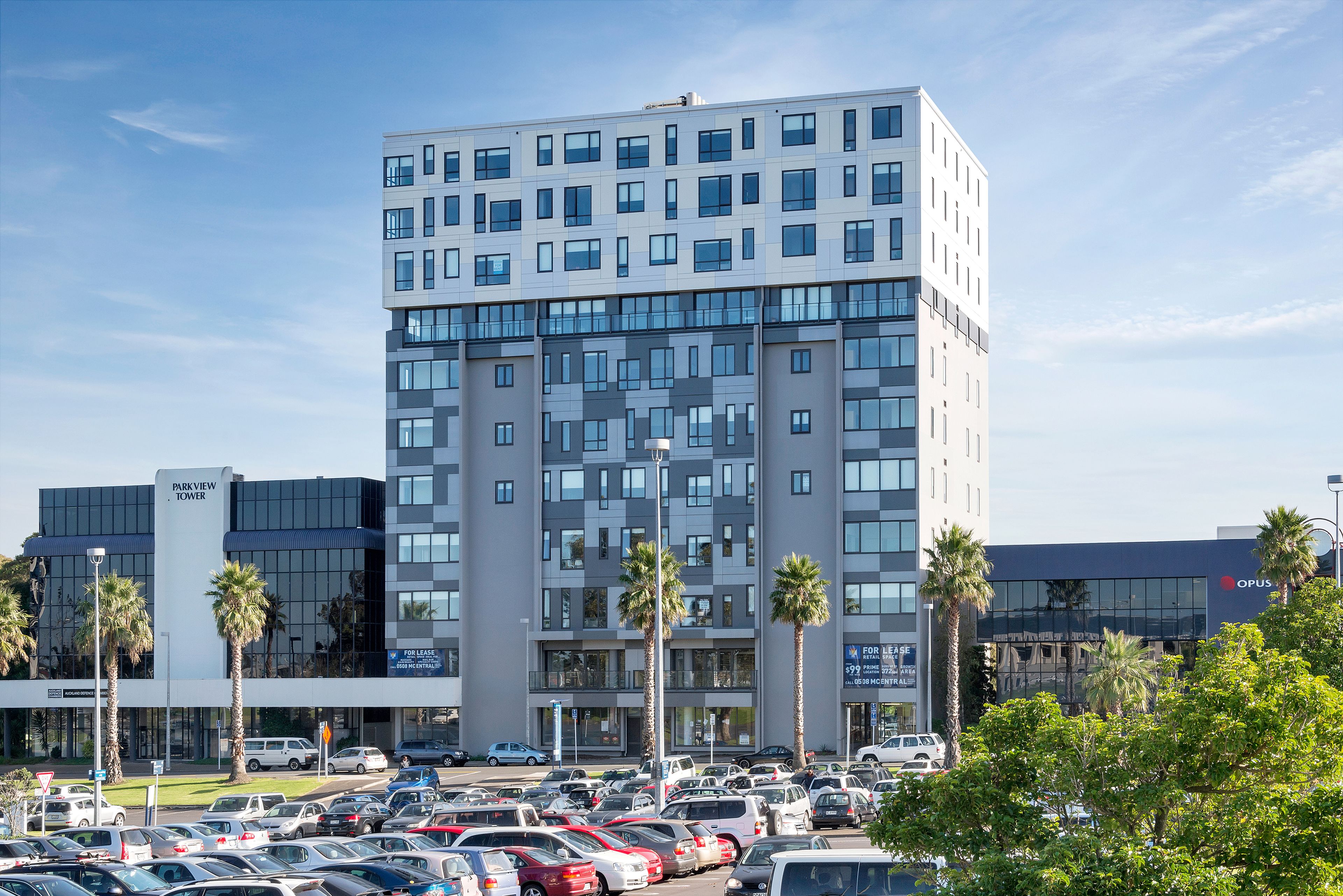 A multi-story building with a modern architectural design, featuring a mix of glass and concrete facades, and surrounded by a parking lot with several cars.