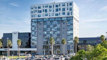 A multi-story building with a modern architectural design, featuring a mix of glass and concrete facades, and surrounded by a parking lot with several cars.