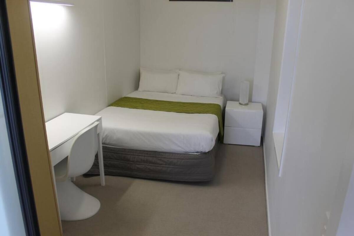A small, clean room with a bed, a desk, and a nightstand.