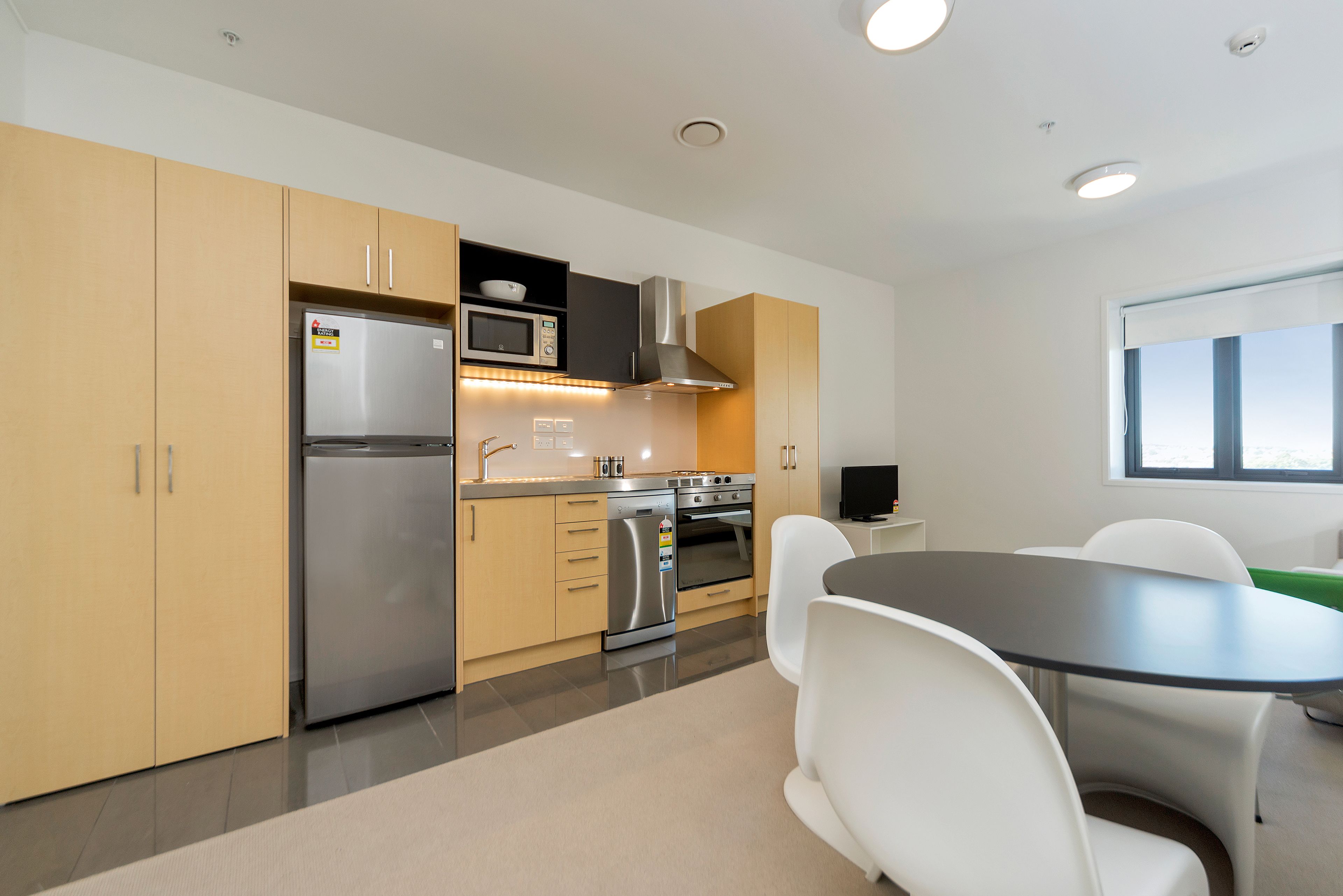 A modern kitchen with stainless steel appliances, wooden cabinets, and a dining area with white chairs.