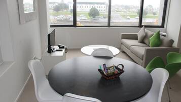 A modern office space with a round table, white chairs, a sofa, and a view of a building through large windows.