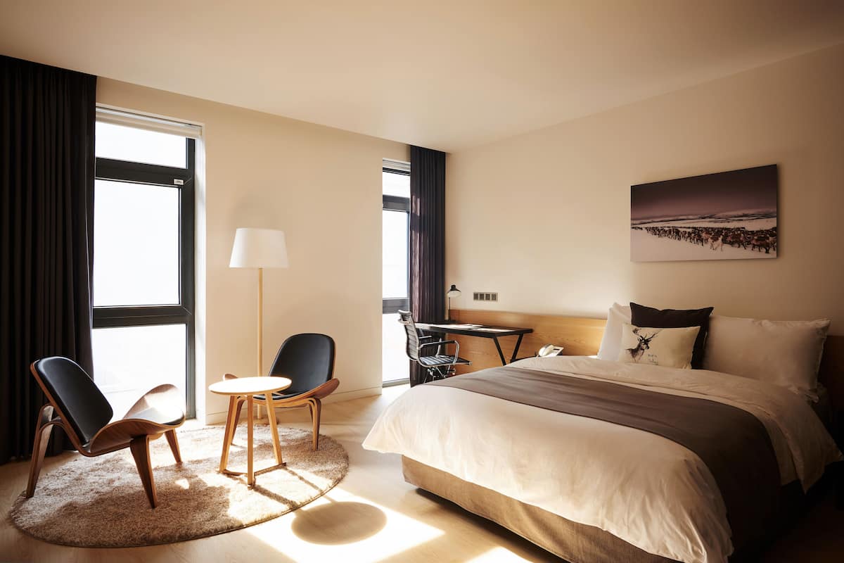 Quarto de hotel com uma cama grande, uma mesa de trabalho, duas cadeiras, uma luminária e um quadro na parede.