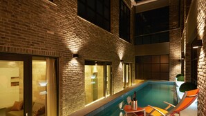 Una piscina interior con pared de ladrillo y puertas de cristal, una tumbona y una botella de champán.