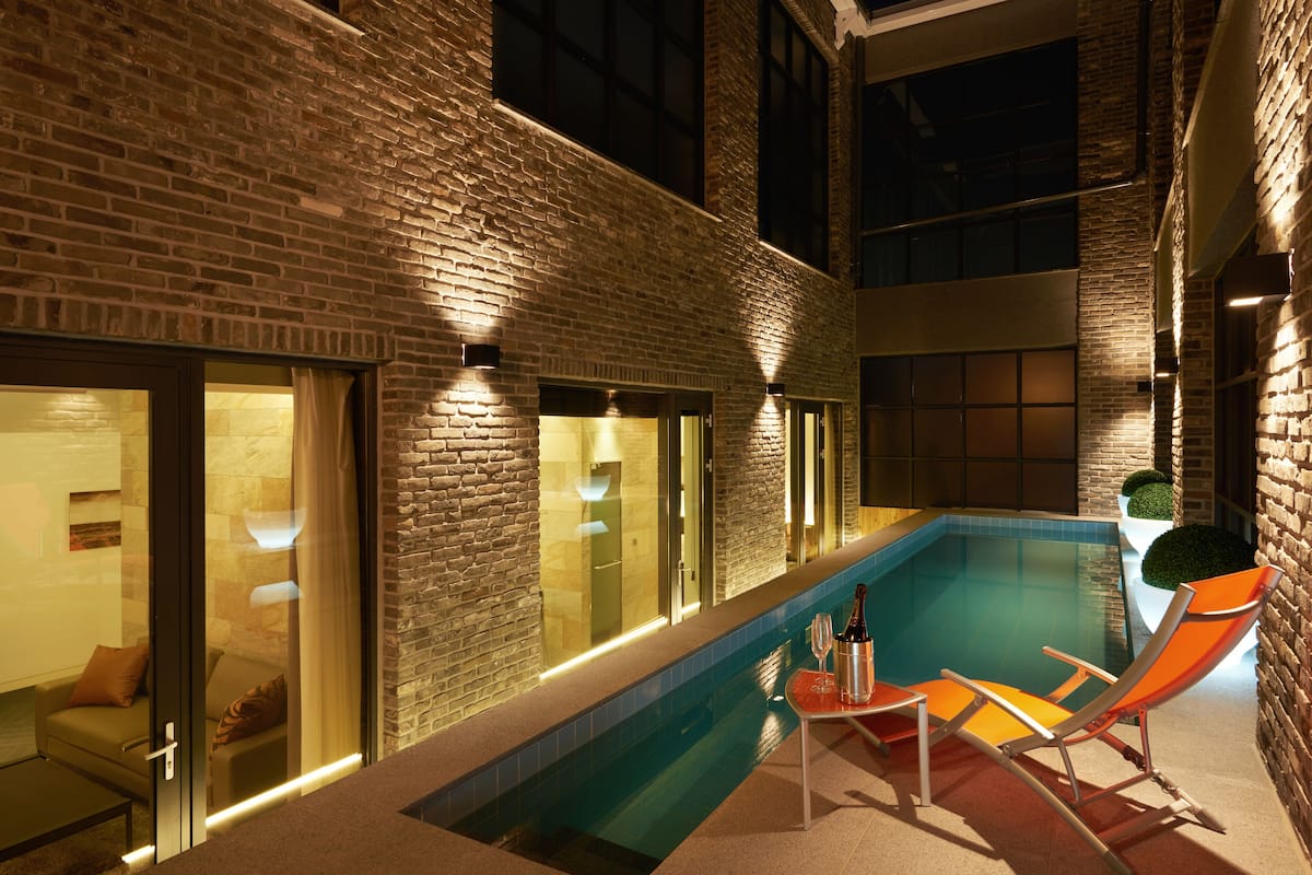 Piscina interna com parede de tijolos, portas de vidro, uma cadeira de lounge e uma garrafa de champanhe.