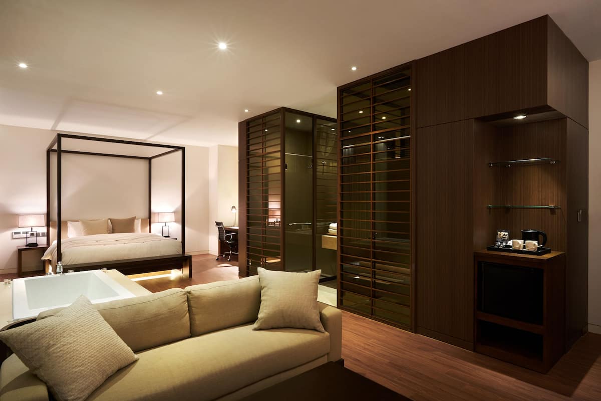Um quarto moderno com uma cama grande, um sofá, um closet espaçoso com portas de vidro e uma pequena mesa com cafeteira.