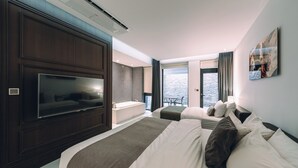 A hotel room with a large TV, a bathtub, and a balcony with a view of the water. - The Classic by Hotelone (Wanju)
