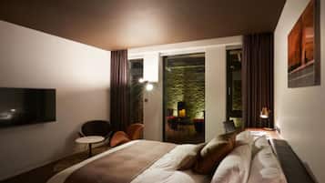 A hotel room with a bed, a TV, a small table, and a chair. There is a balcony with a table and chairs outside the room.