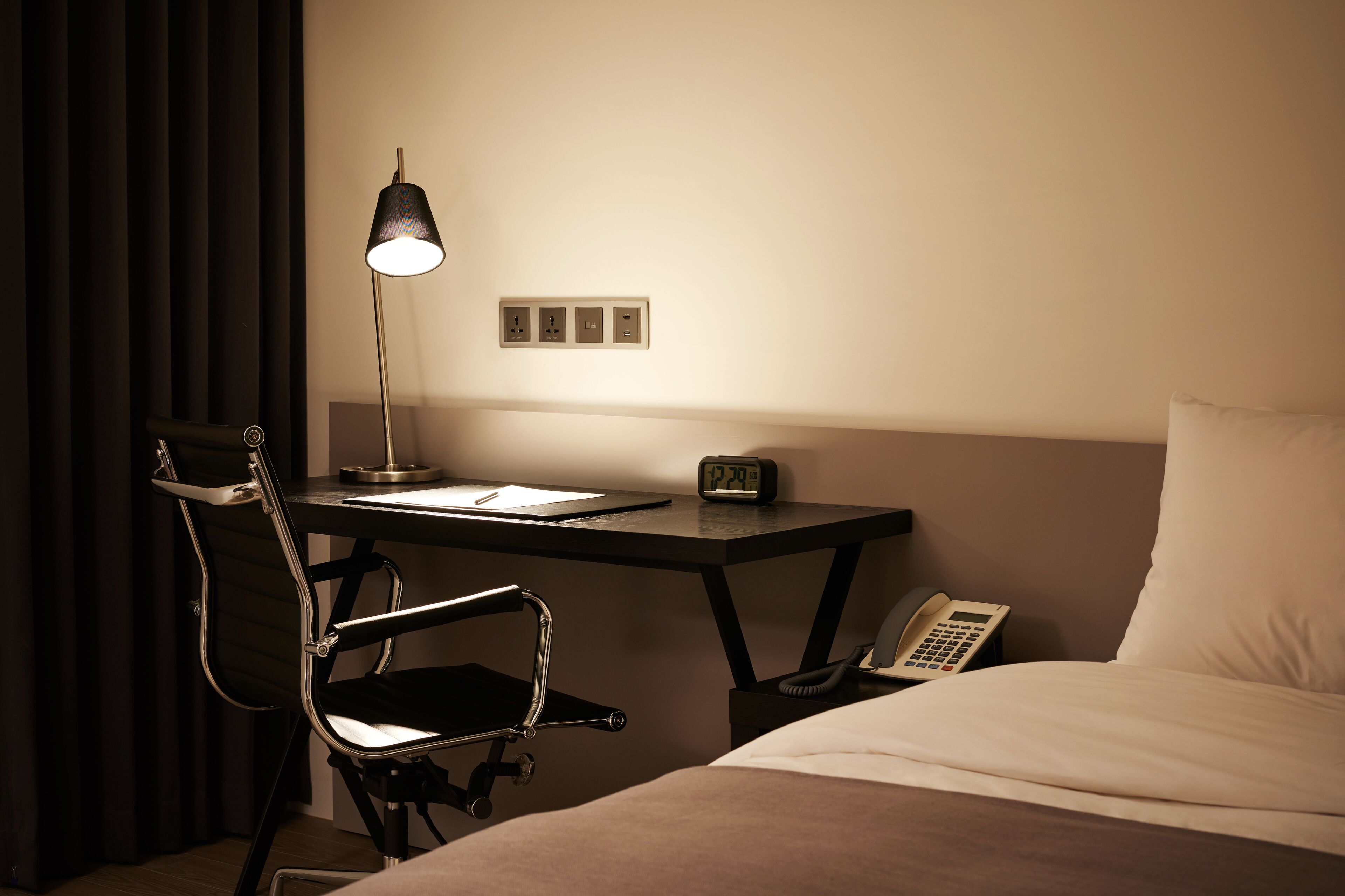Una camera d'albergo con scrivania, sedia, lampada, sveglia, telefono e letto.