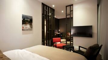 Una habitación de hotel moderna con una cama grande, un televisor de pantalla plana en la pared, un escritorio con una silla y un sillón rojo.