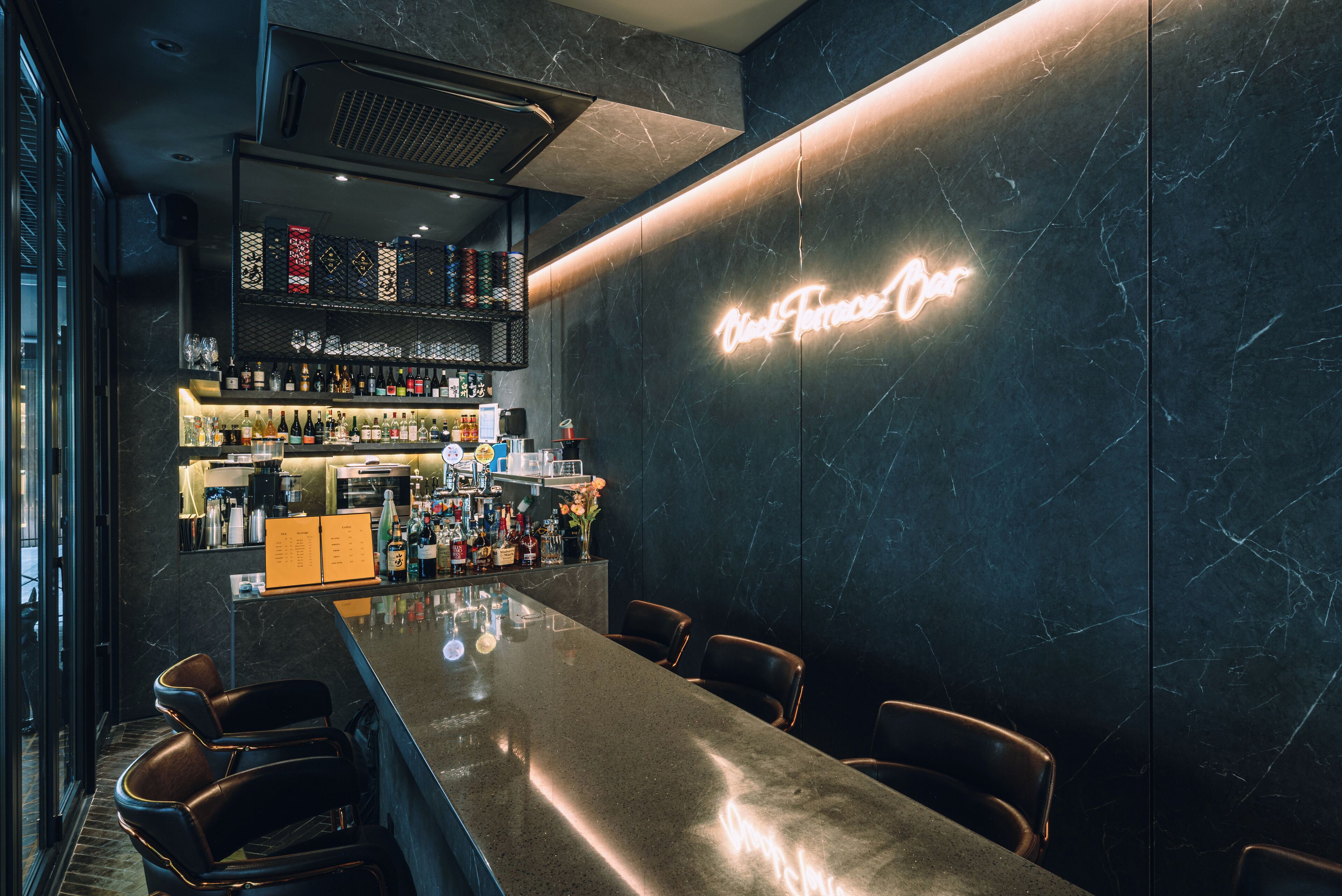 A modern bar area with a marble countertop, bar stools, and a neon sign.