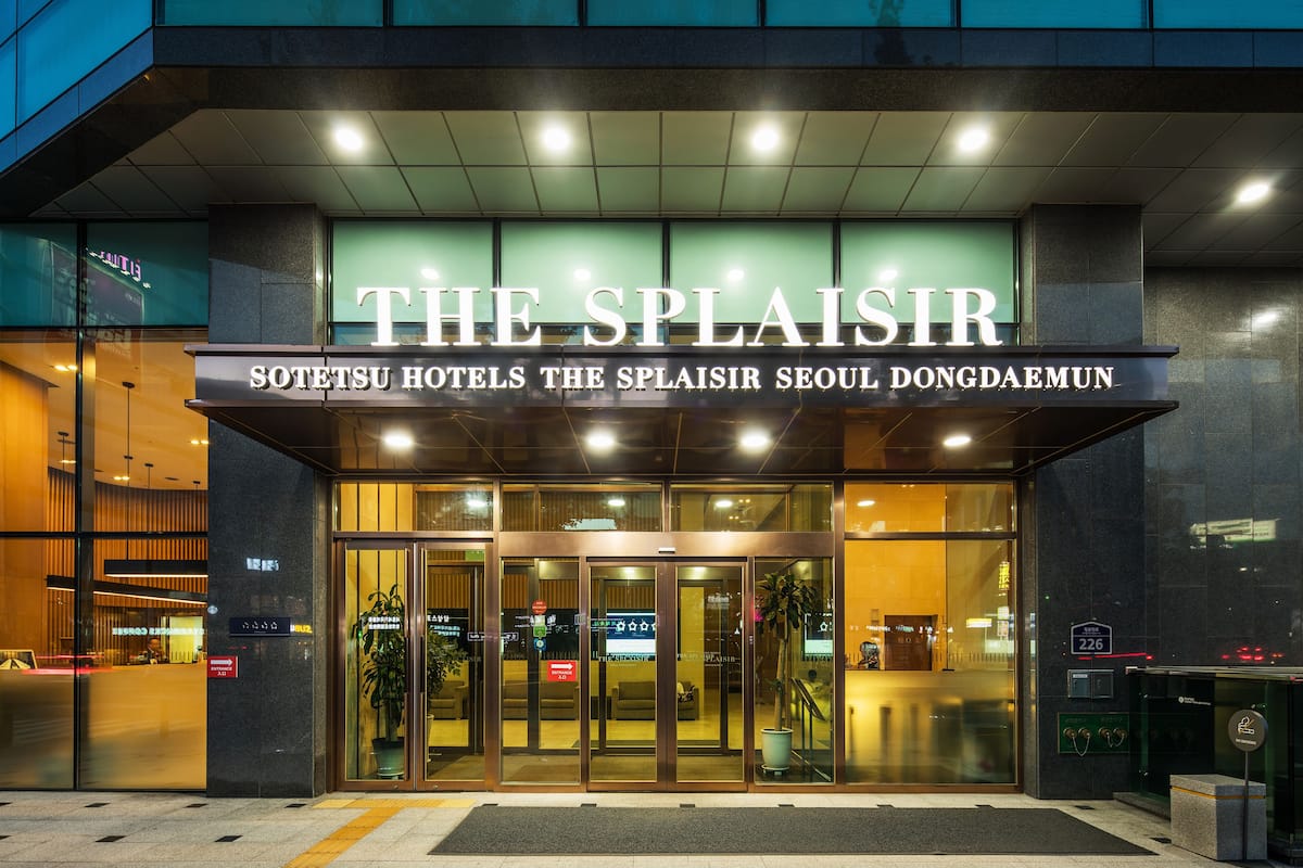 The entrance of The Slaisir hotel with a modern glass facade and illuminated signage.