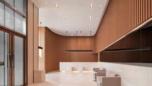 A modern reception area with a curved ceiling, recessed lighting, a reception desk, and a seating area with sofas. - Sotetsu Hotels The Splaisir Seoul Dongdaemun (Seoul)