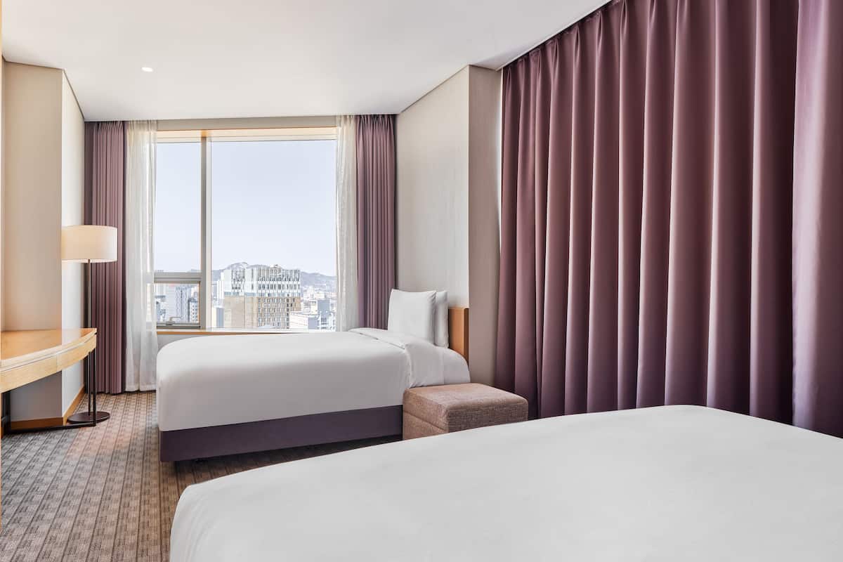 A hotel room with two beds, a desk, and a view of the city.