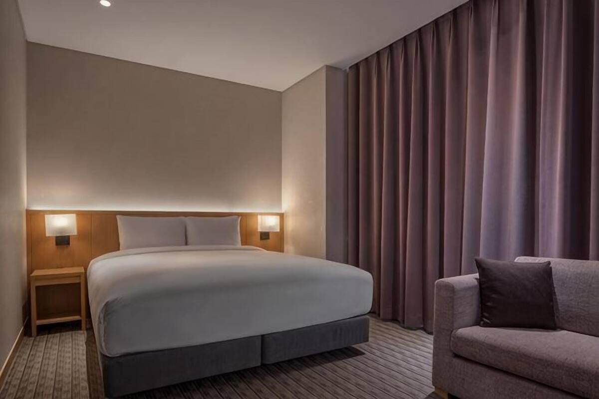 A hotel room with a large bed, bedside lamps, a sofa, and a curtain-covered window.