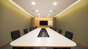 A conference room with a long table, chairs, and a projector screen.