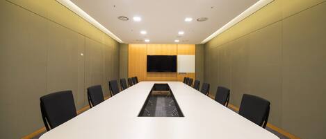 A conference room with a long table, chairs, and a projector screen.