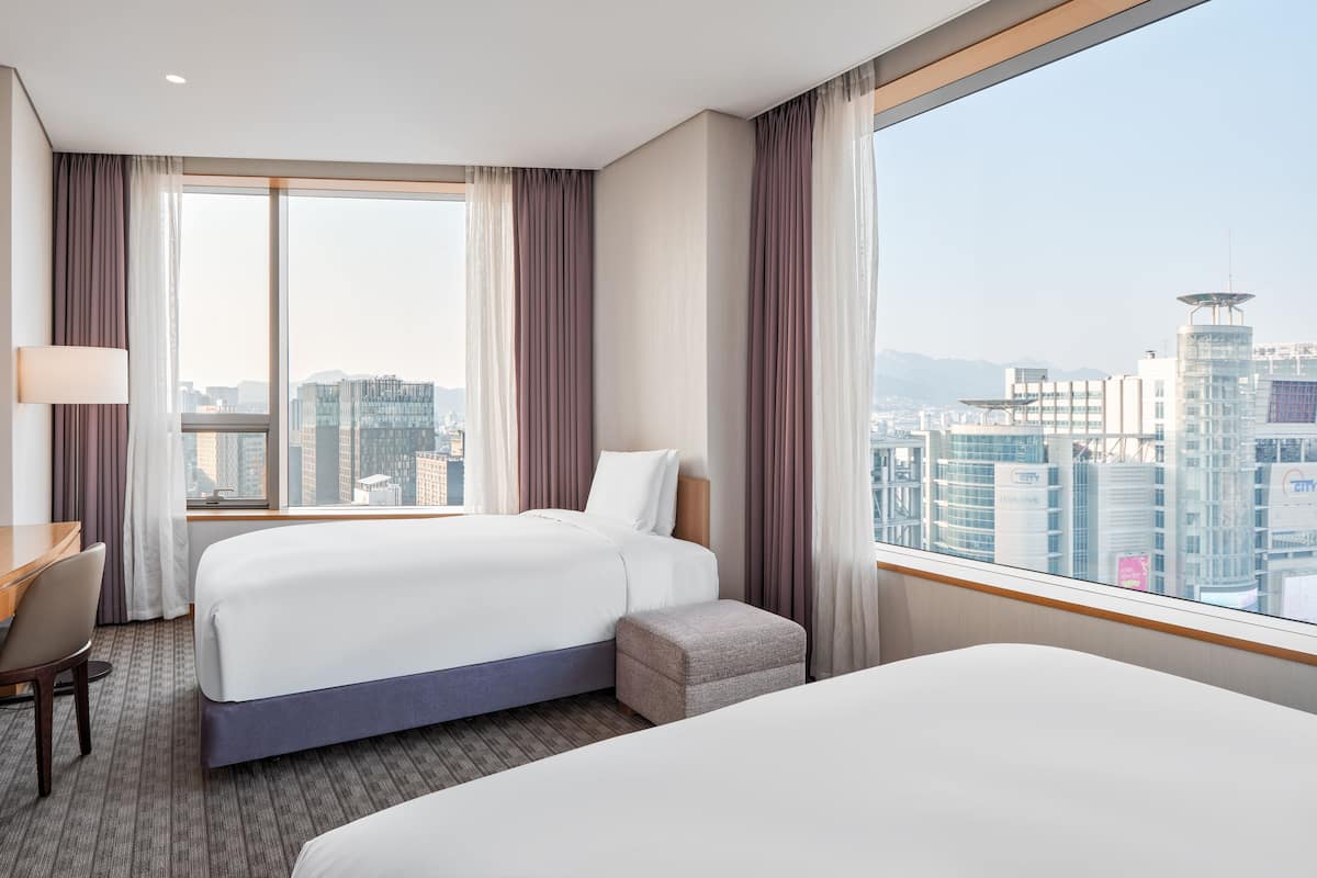 A hotel room with a large bed, a smaller bed, a desk, and a view of the cityscape.