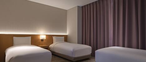 Una habitación de hotel con dos camas, una mesita de noche, una lámpara fijada a la pared y un ventanal con cortinas.