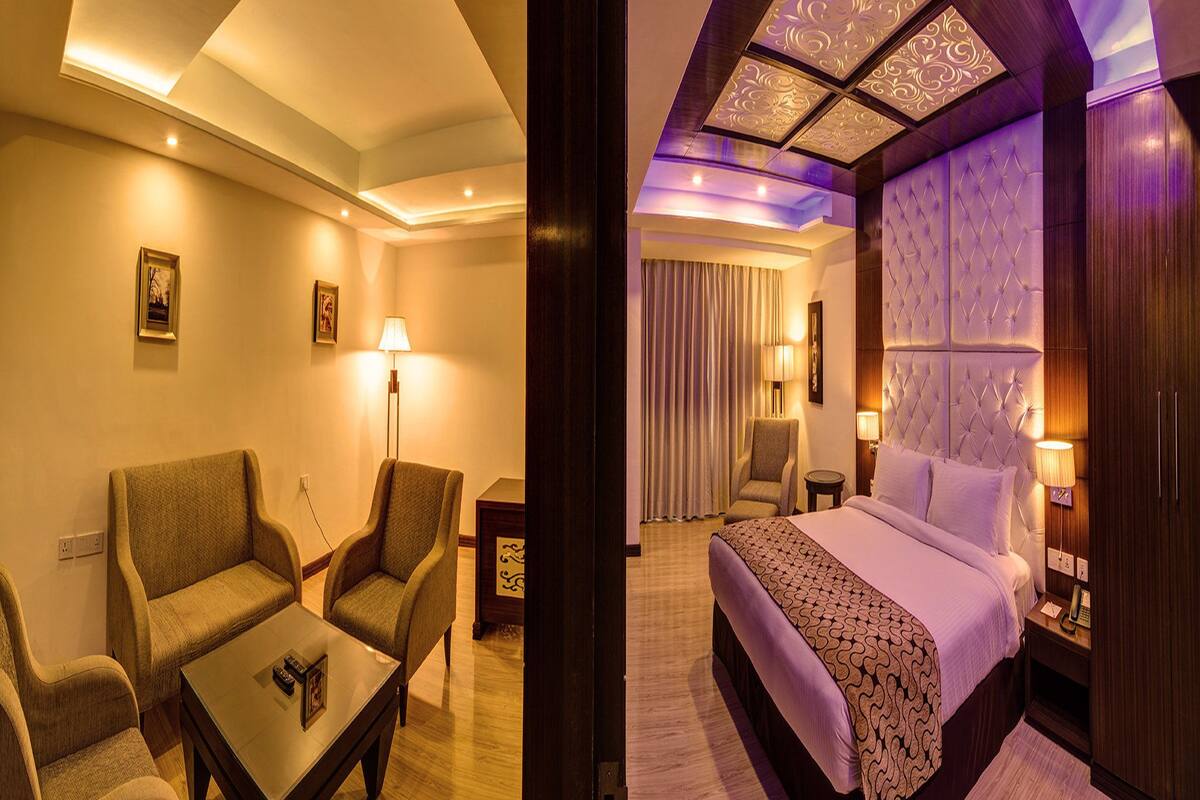 Una habitación de hotel con una cama, dos sillones, una mesita, una lámpara y una mesita de noche.