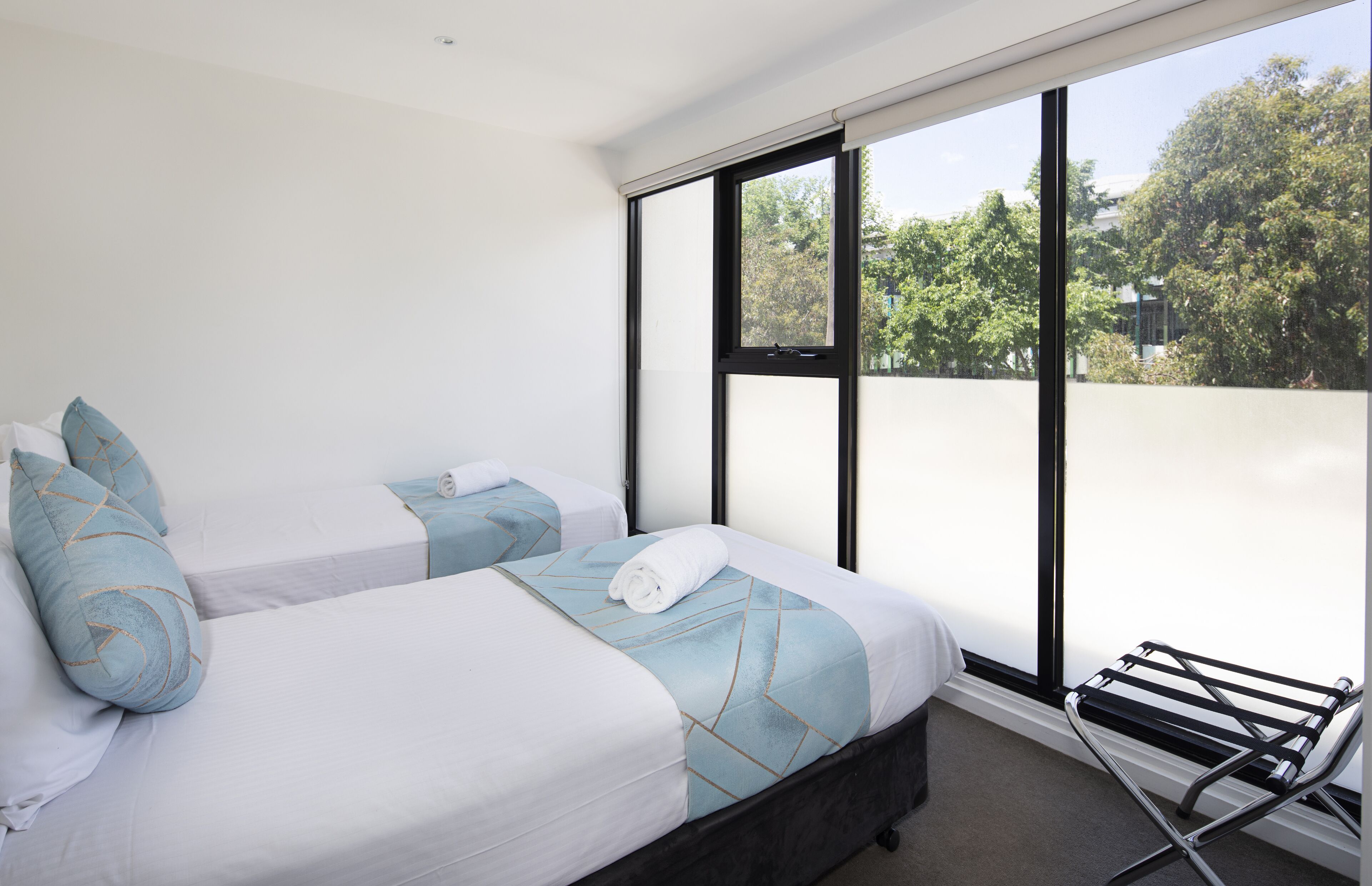 A hotel room with two beds, a large window, and a black metal drying rack.
