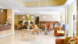 A hotel lobby with a reception desk, seating area, and a staircase leading to an upper floor.