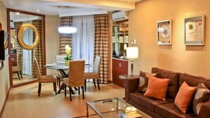 A modern living room with a brown leather sofa, a glass coffee table, and a dining area with a round table and chairs.