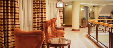 A lobby with striped curtains, a round glass table, and orange chairs.