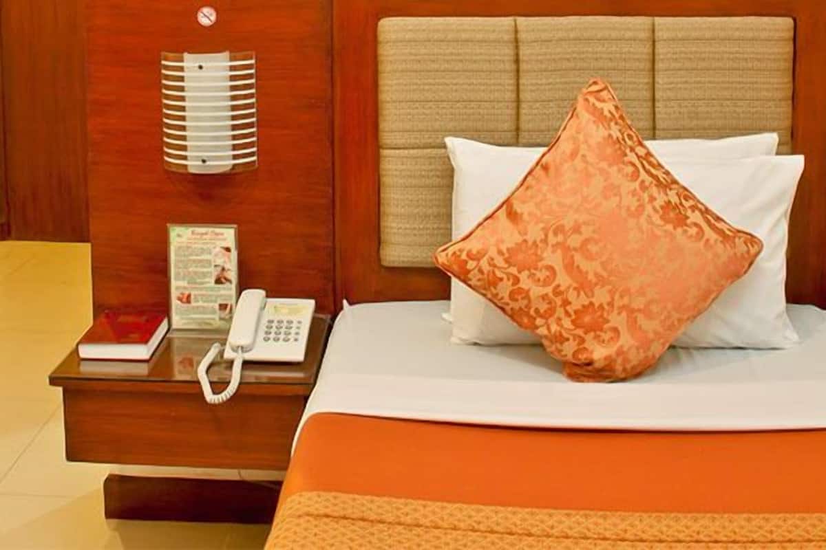 A hotel room with a wooden nightstand, a telephone, a bed with an orange bedspread, and a patterned pillow.