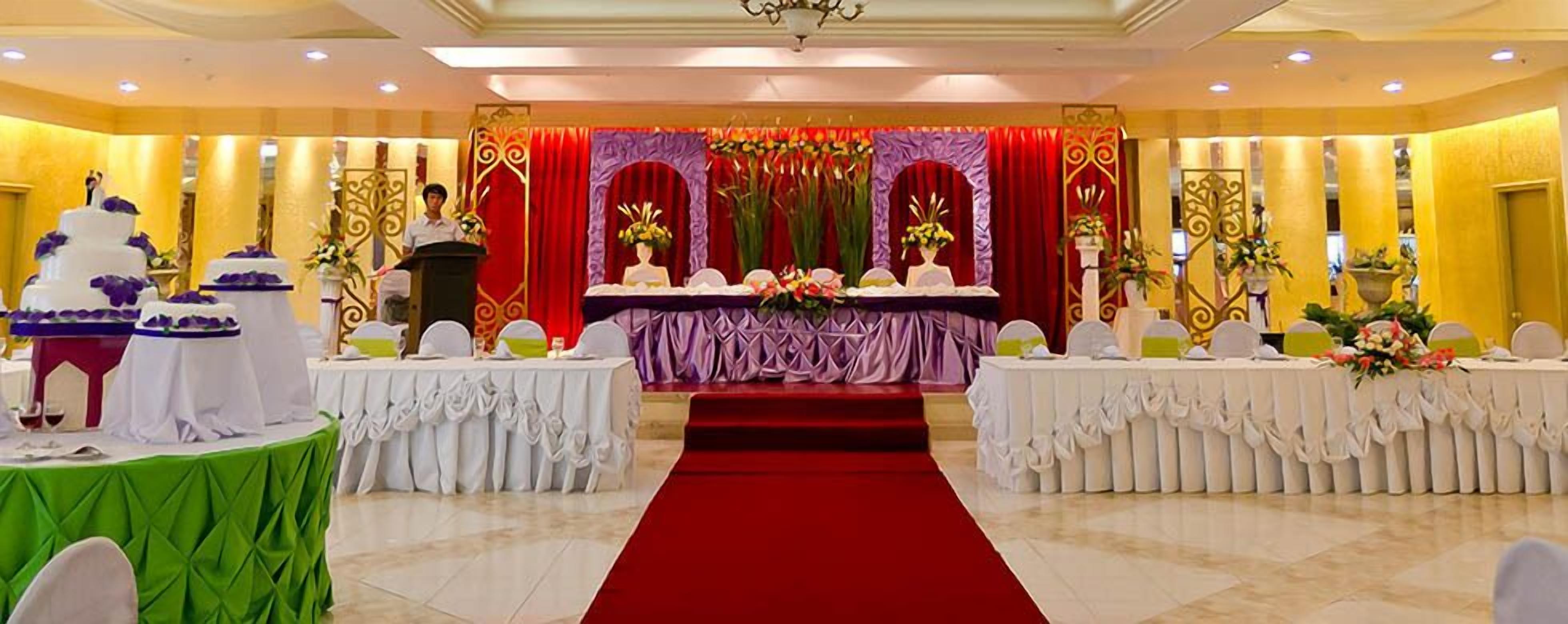 A banquet hall with a red carpet, white tables, and a stage with red curtains.