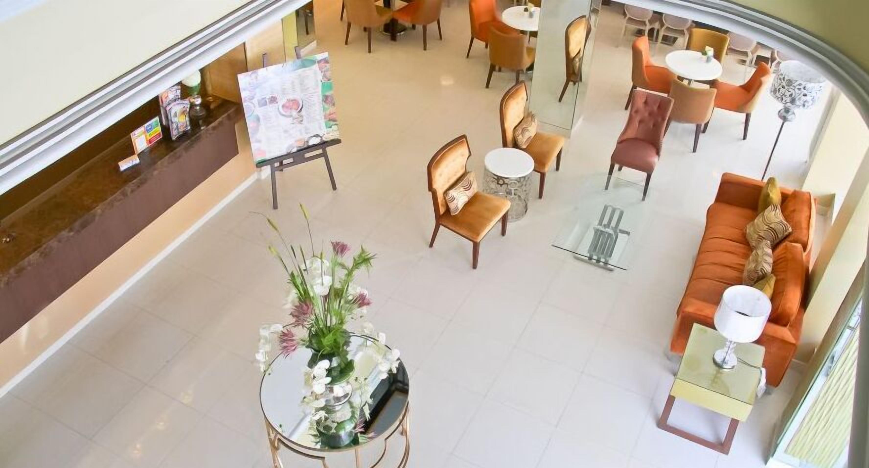 A hotel lobby with a central seating area, a reception desk, and a glass coffee table with a floral arrangement.