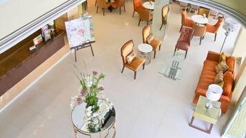 A hotel lobby with a central seating area, a reception desk, and a glass coffee table with a floral arrangement.
