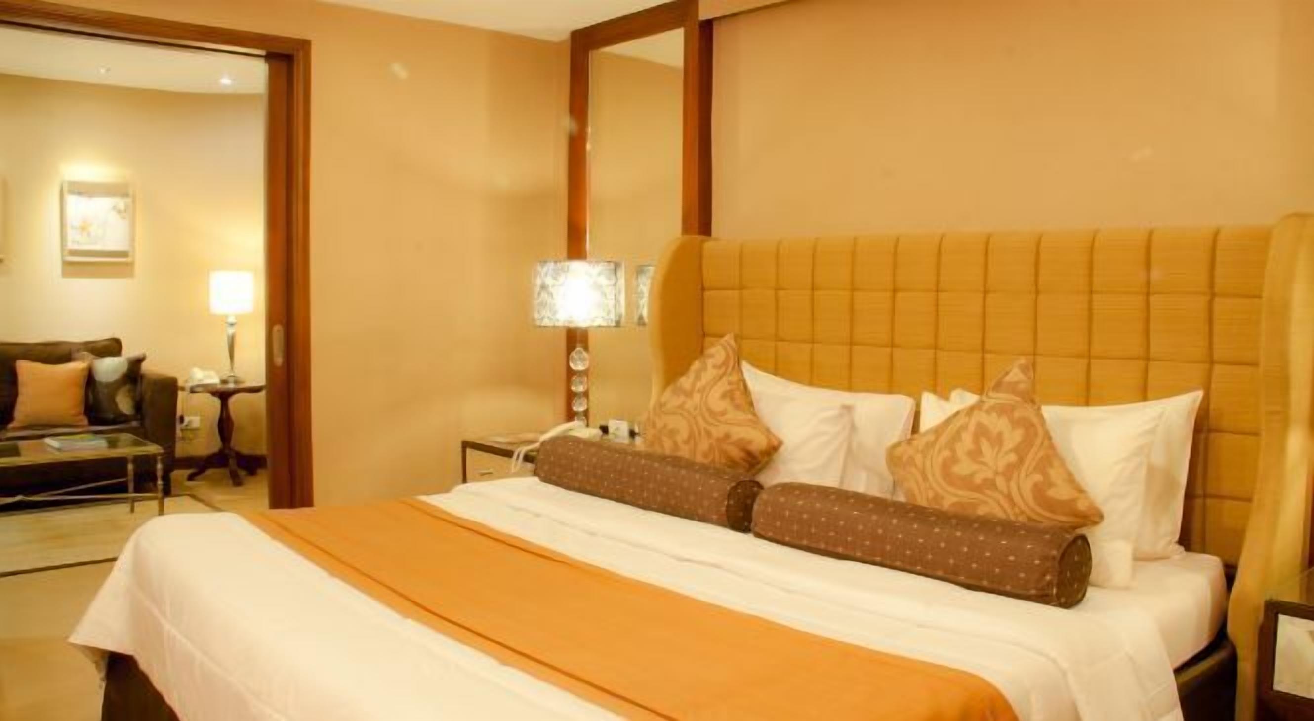 A hotel room with a large bed, a nightstand with a lamp, a chair, and a mirror.