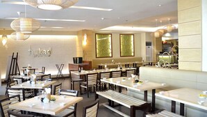 A restaurant interior with multiple dining tables and benches, a visible counter area, and hanging light fixtures.