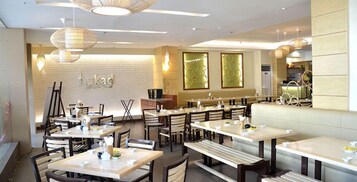 Interior de restaurante com várias mesas e bancos, área de balcão visível e luminárias pendentes.