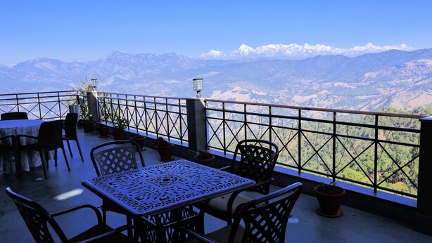 A terrace with a table and chairs, overlooking a mountainous landscape. - ECKO Woodsvilla Resort (Ranikhet)