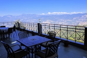 A terrace with a table and chairs, overlooking a mountainous landscape. - ECKO Woodsvilla Resort (Ranikhet)