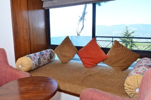 A seating area with a view of mountains through a window. - ECKO Woodsvilla Resort (Ranikhet)