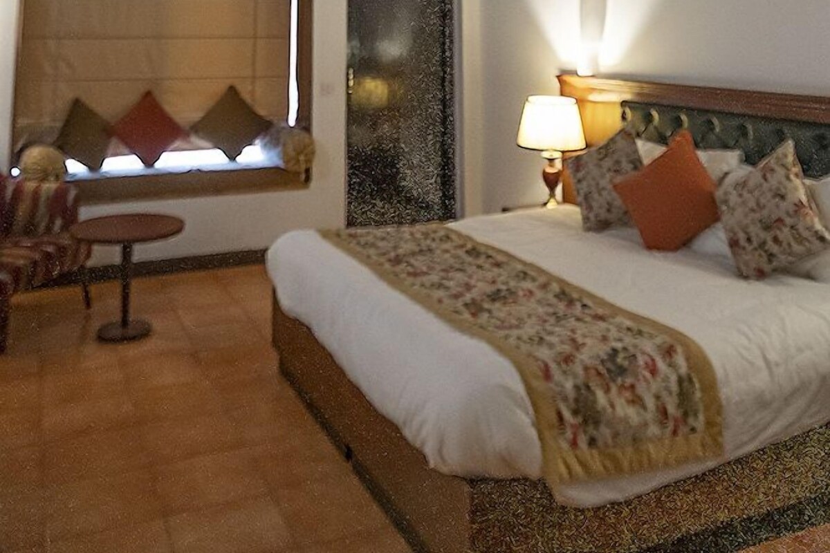 A bedroom with a wooden ceiling, a bed with pillows, a bedside table, and a window with blinds.