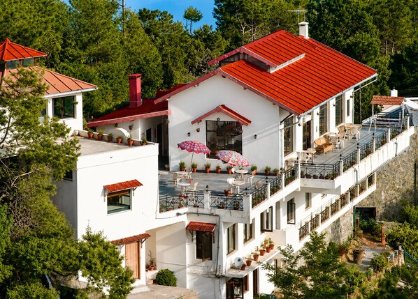 A multi-story building with a red roof, balconies, and outdoor seating areas. - ECKO Woodsvilla Resort (Ranikhet)