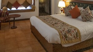 A bedroom with a wooden ceiling, a bed with a floral bedspread, a bedside lamp, and a window with blinds. - ECKO Woodsvilla Resort (Ranikhet)