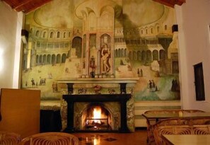 A room with a fireplace, a mural on the wall, and wicker furniture. - Woodsvilla Residency Ranikhet (Ranikhet)