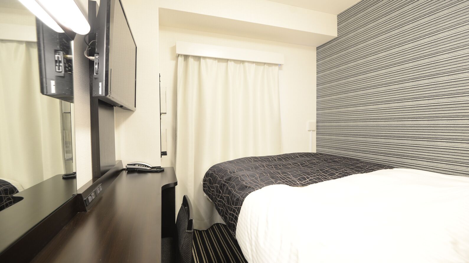 Een hotelkamer met een bed, bureau, telefoon en televisie.