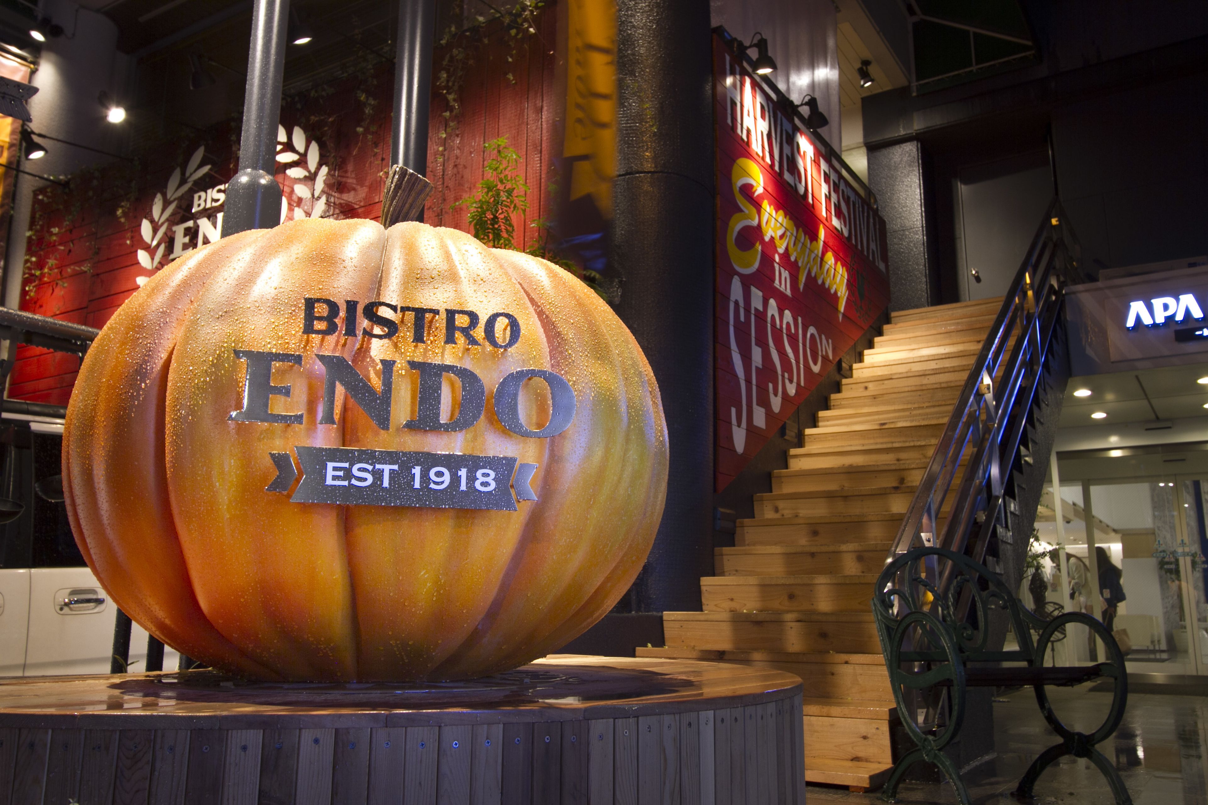Une grosse citrouille sur laquelle on peut lire « BISTRO ENDO EST 1918 », le tout posé sur une plateforme en bois.