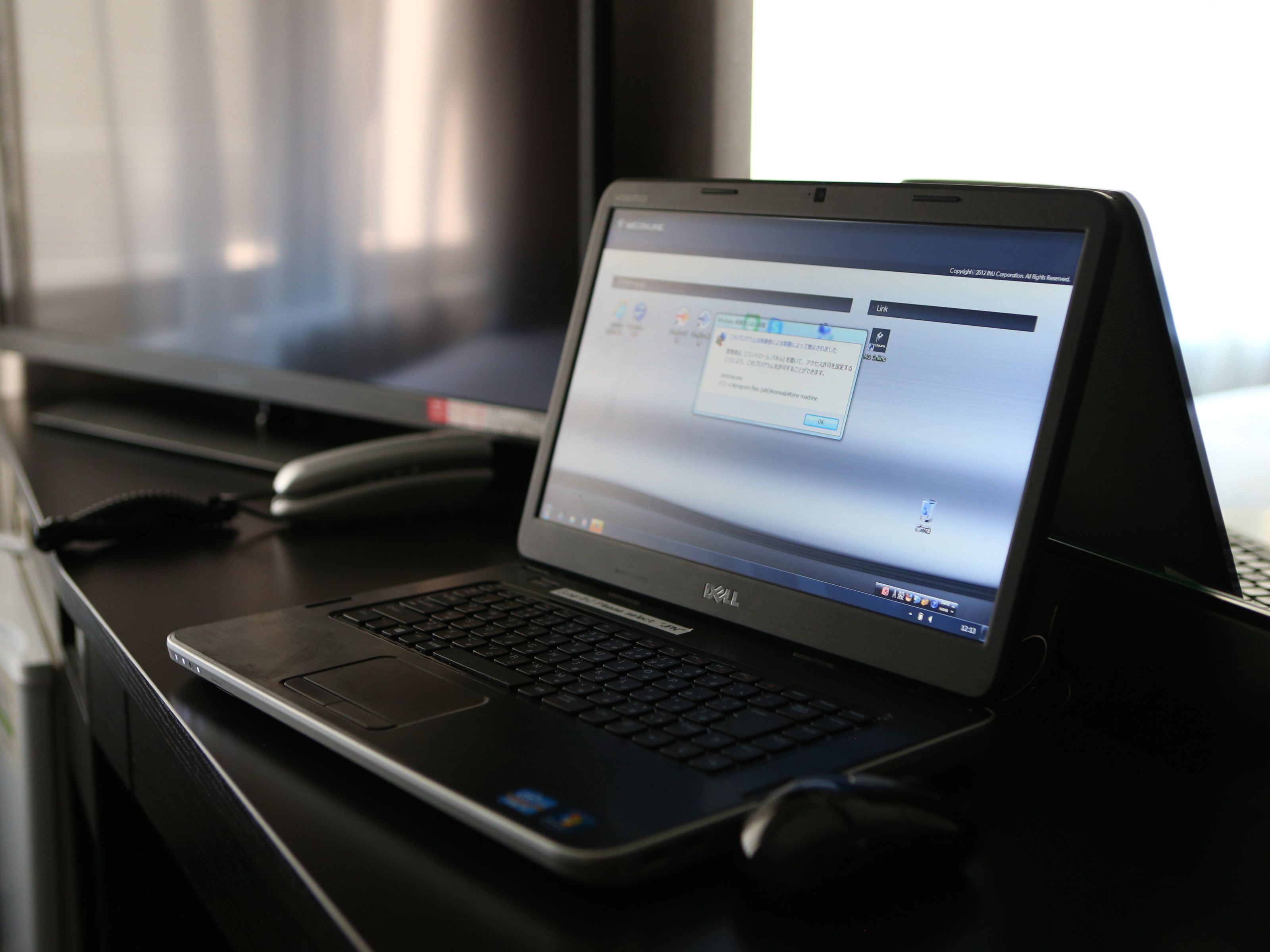 Een laptop op een bureau, met een monitor op de achtergrond.