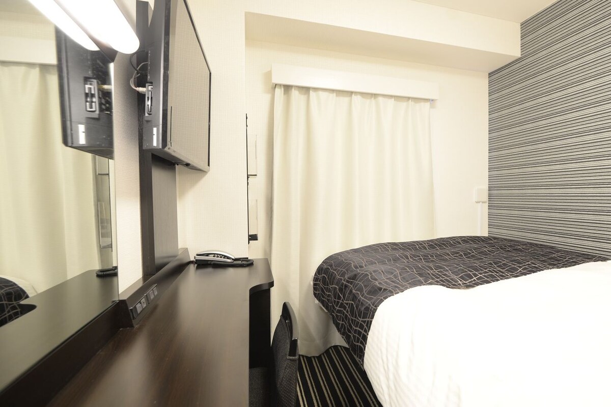 A hotel room with a bed, a desk, a telephone, and a television.