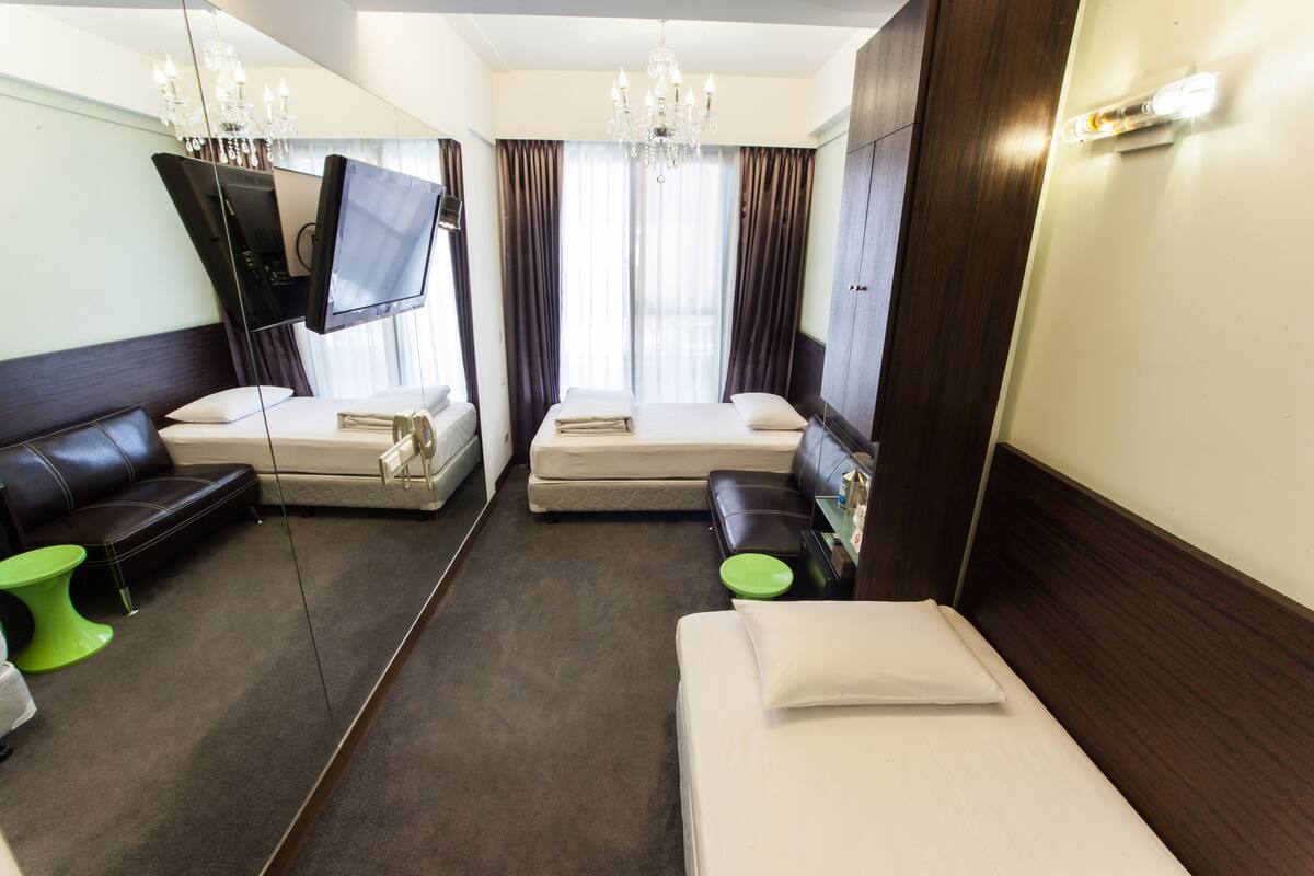 Una habitación de hotel con una cama grande, una cama más pequeña, un sofá, un televisor montado en la pared y una araña.