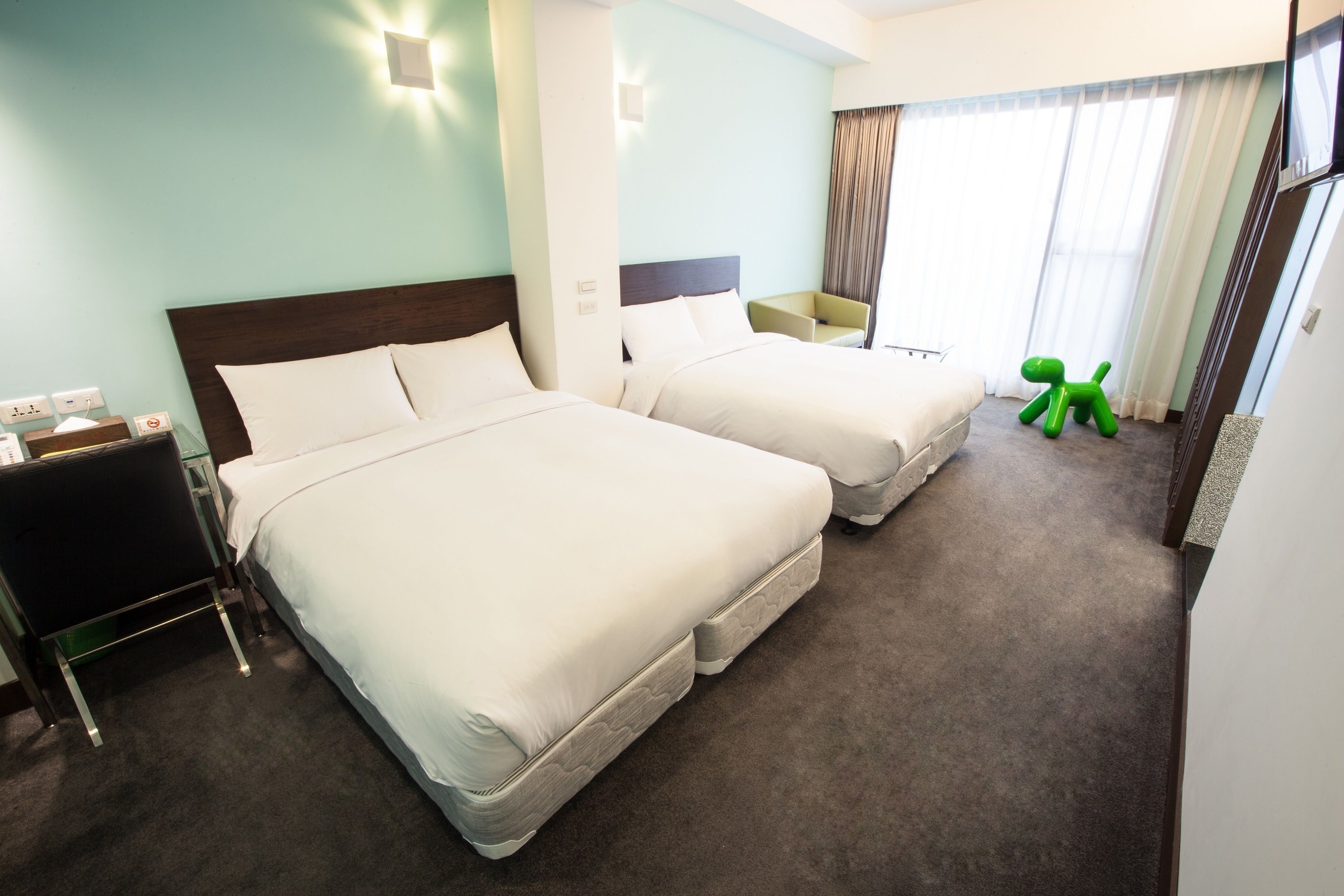 A hotel room with two beds, a desk, a chair, and a green toy.