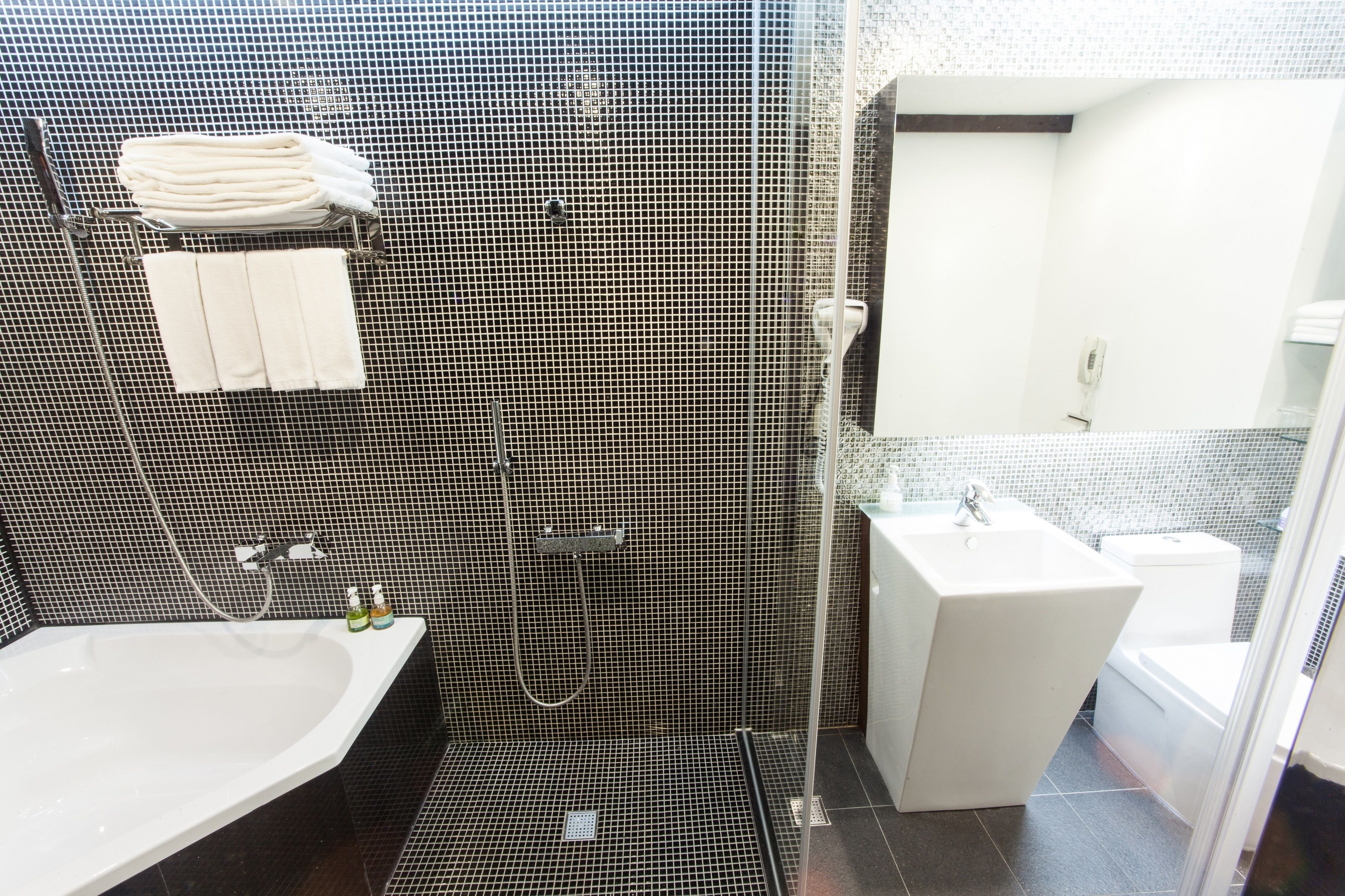 Un baño moderno con pared de azulejos blanco y negro, un lavabo blanco, zona de ducha y un inodoro.